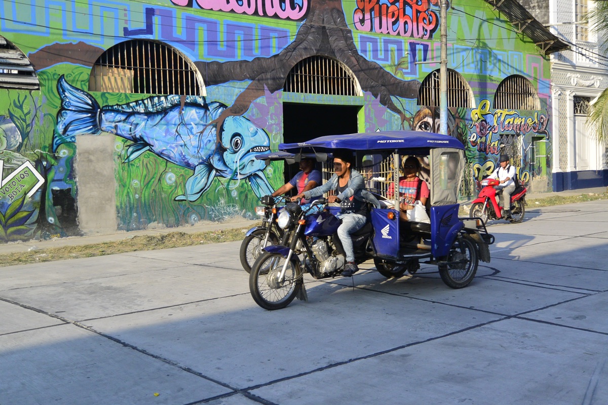 Motorcycle taxi passing a colorful street mural